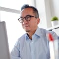 Person in blue button-down and glasses works in an office on a desktop computer.